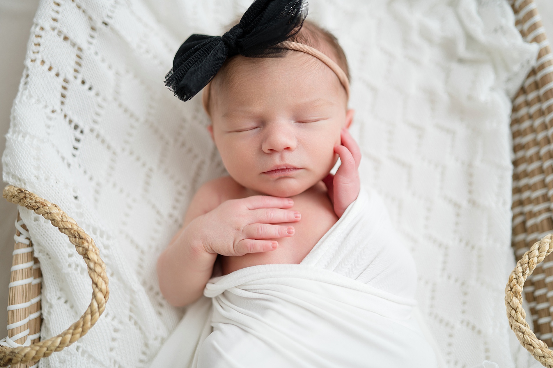 newborn girl wrapped in white blanket wearing black bow