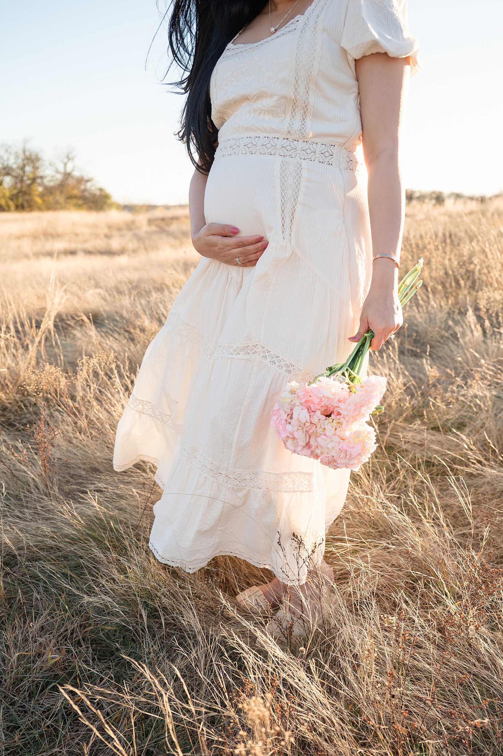 expectant mom holds fresh flowers while cradling baby bump