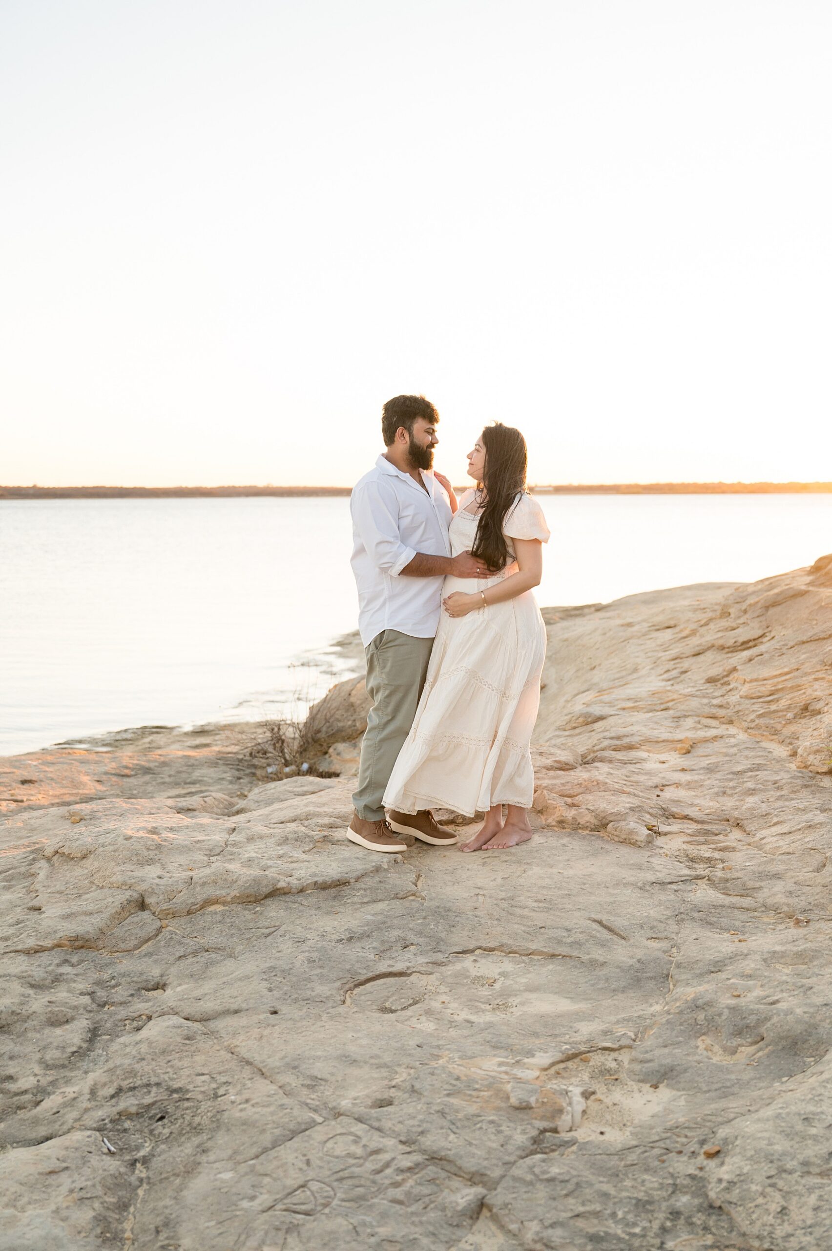 couple on rocky beach by the water during Flower Mound, TX maternity session