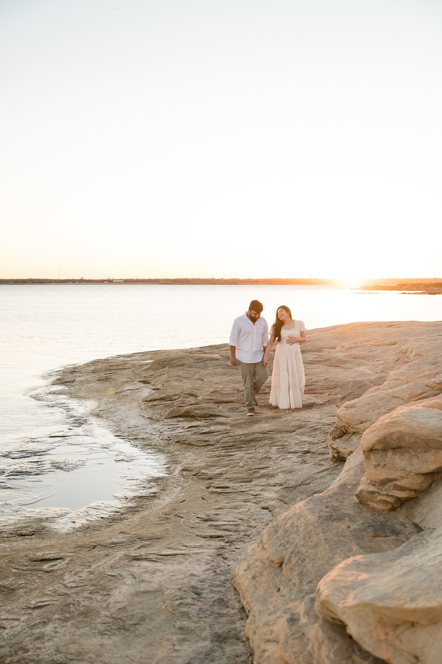 couple hold hands as they walk along the beach at sunset
