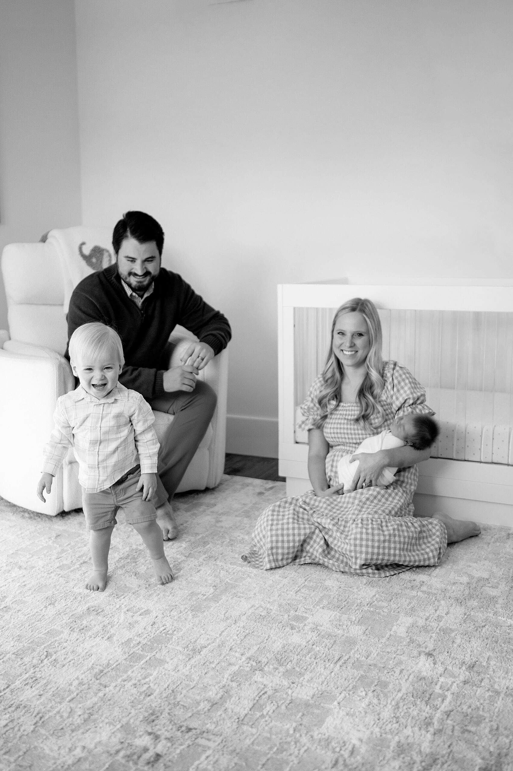 mom holding newborn as big brother laughs and walks around the room 