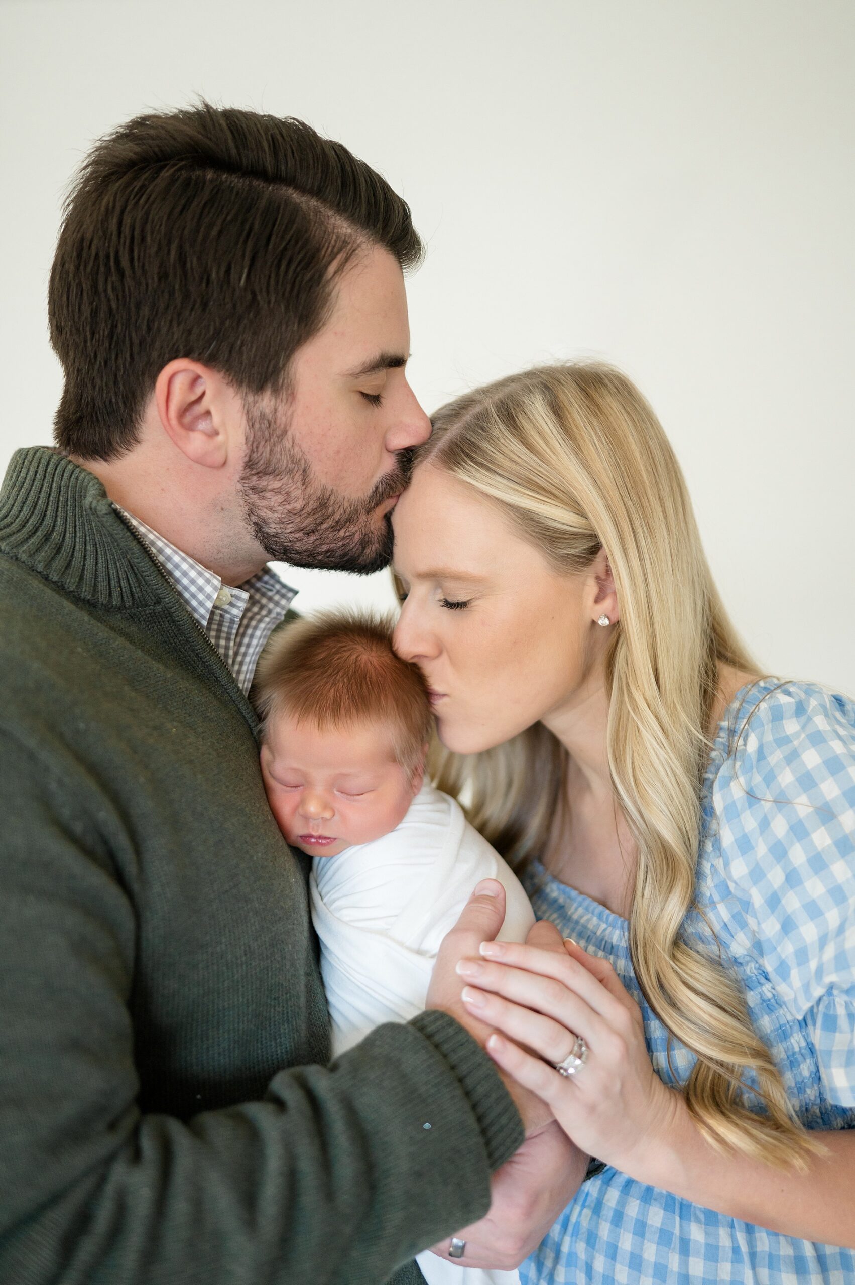 dad kisses mom's head as she kisses baby's head in sweet newborn photo 