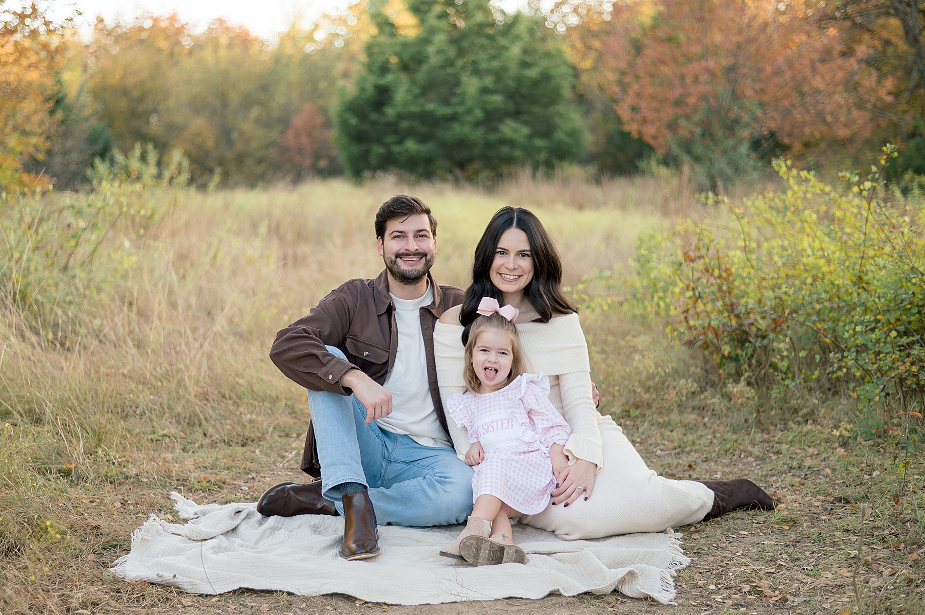 family of three sits on blanket during maternity announcement 