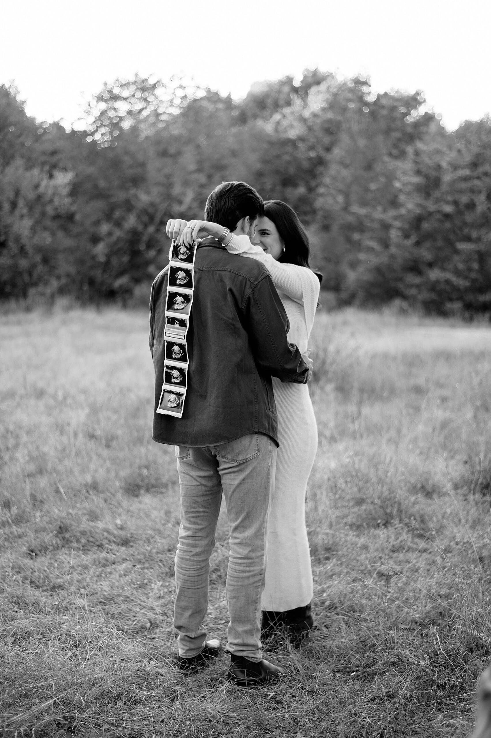 husband and wife hug while wife holds ultrasound photo 