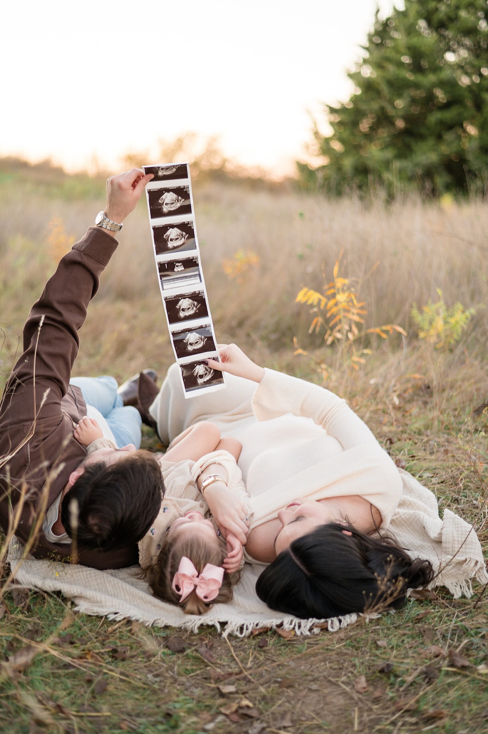 Arbor Hills Maternity announcement  with family laying on blanket looking up at ultrasound photo